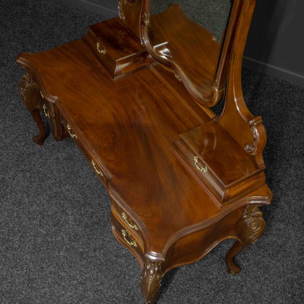A Victorian carved mahogany dressing table featuring a central swing mirror, small upper jewellery drawers, lower storage drawers, and carved cabriole legs. View V