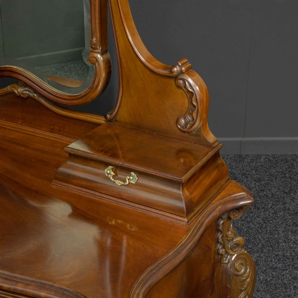 A Victorian carved mahogany dressing table featuring a central swing mirror, small upper jewellery drawers, lower storage drawers, and carved cabriole legs. View VI