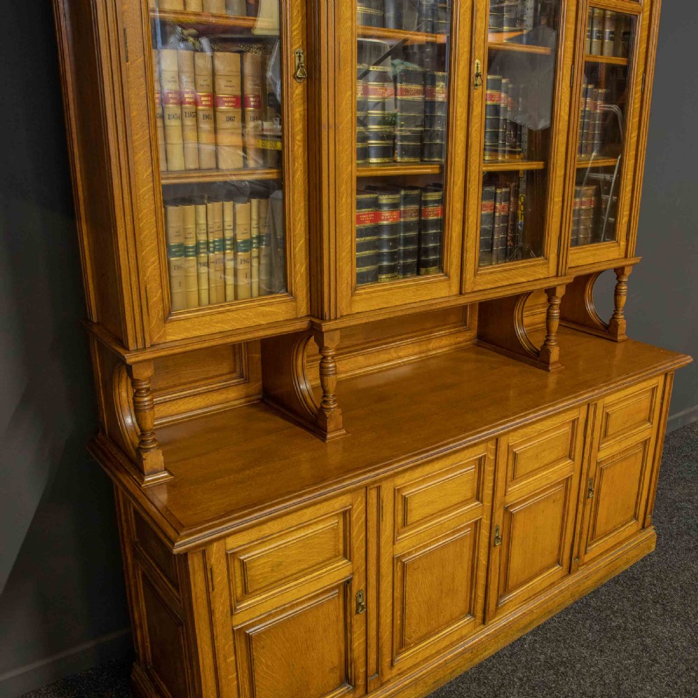 An Edwardian golden oak glazed bookcase featuring a swan-neck pediment, leaded glass doors with stained glass roundels, and a four-door cupboard base. View IV