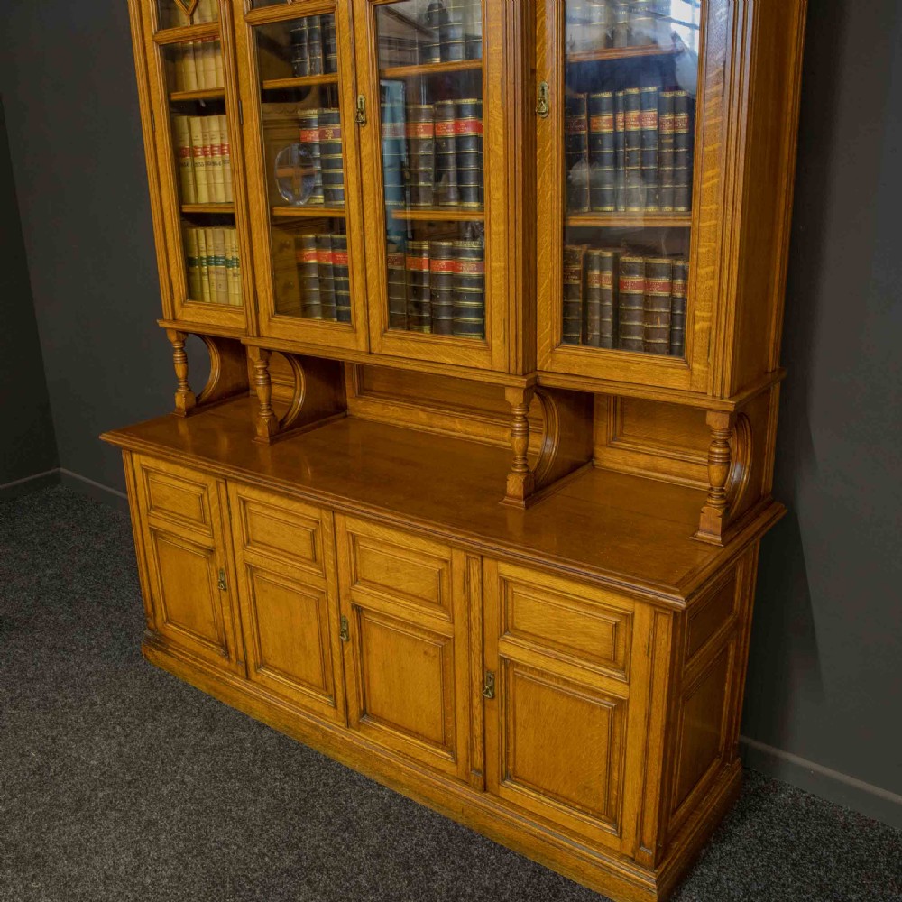 An Edwardian golden oak glazed bookcase featuring a swan-neck pediment, leaded glass doors with stained glass roundels, and a four-door cupboard base. View V