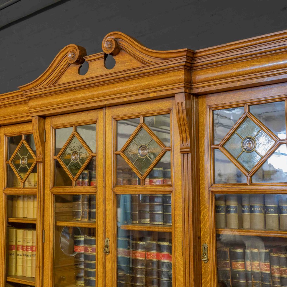 An Edwardian golden oak glazed bookcase featuring a swan-neck pediment, leaded glass doors with stained glass roundels, and a four-door cupboard base. View VIII