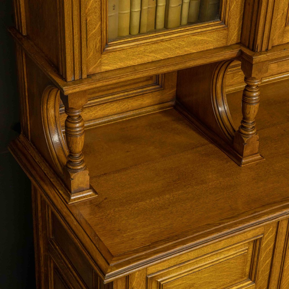 An Edwardian golden oak glazed bookcase featuring a swan-neck pediment, leaded glass doors with stained glass roundels, and a four-door cupboard base. View X