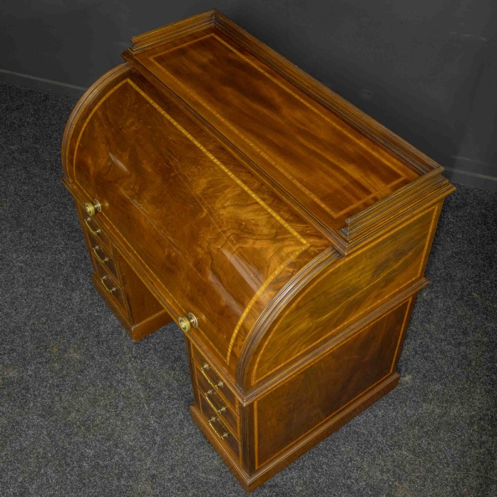 A Sheraton Revival mahogany cylinder desk featuring satinwood crossbanding, twin drawer pedestals, and an extended writing surface fitted with blue leather. View VI