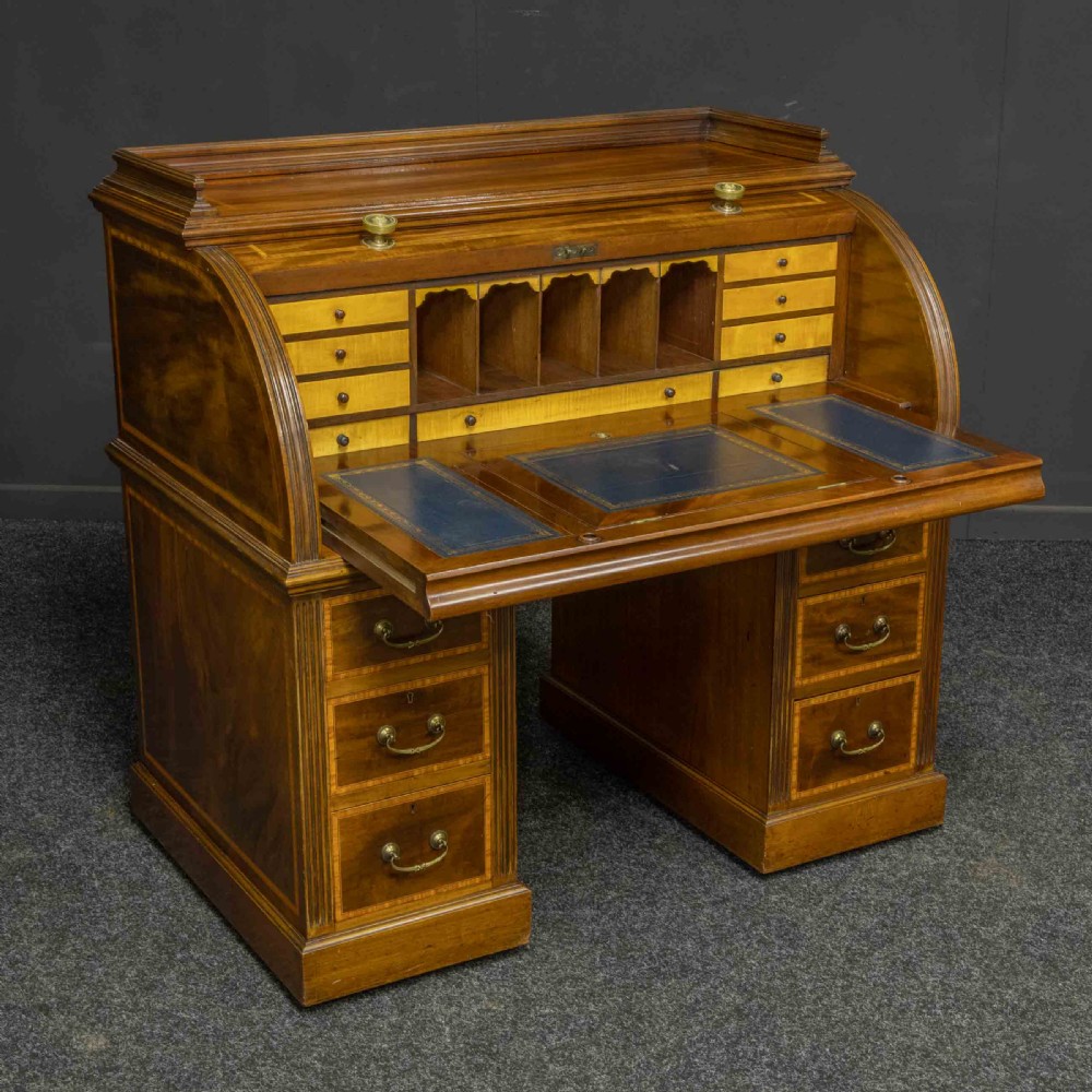 A Sheraton Revival mahogany cylinder desk featuring satinwood crossbanding, twin drawer pedestals, and an extended writing surface fitted with blue leather. View XIV