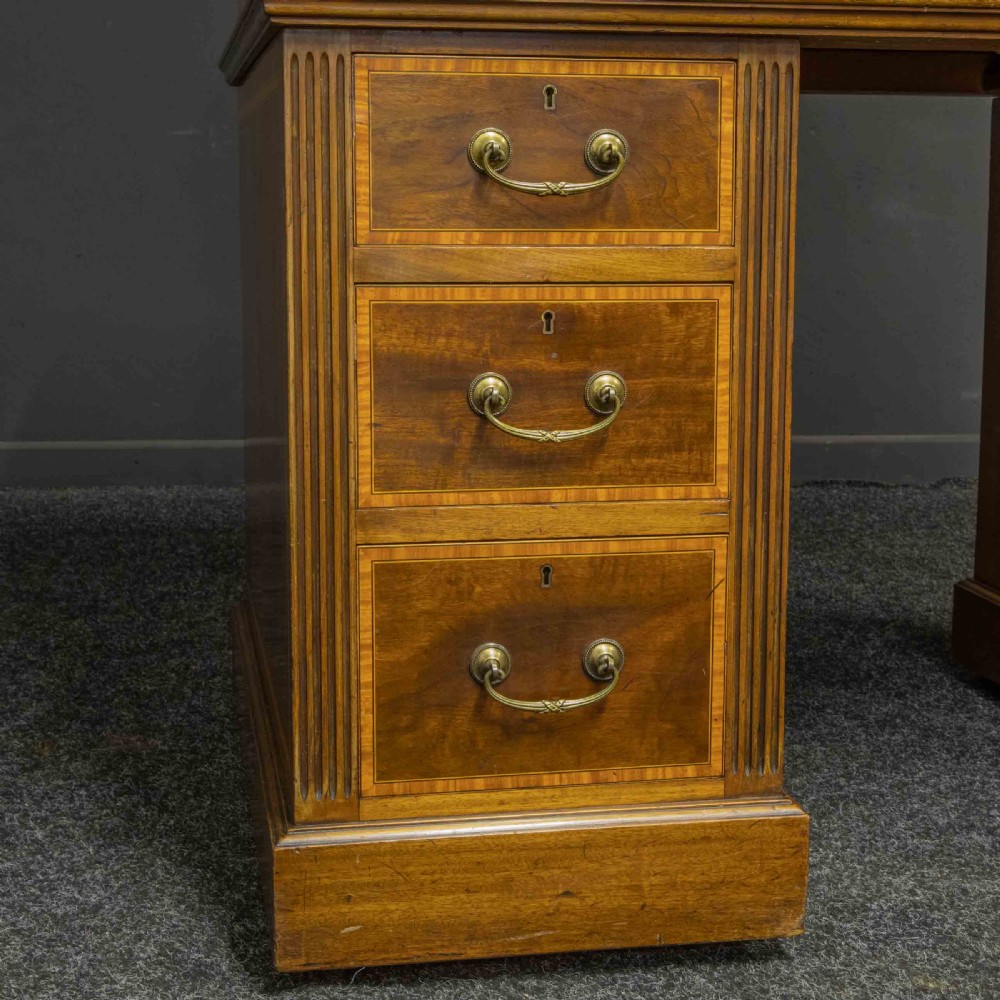 A Sheraton Revival mahogany cylinder desk featuring satinwood crossbanding, twin drawer pedestals, and an extended writing surface fitted with blue leather. View XV