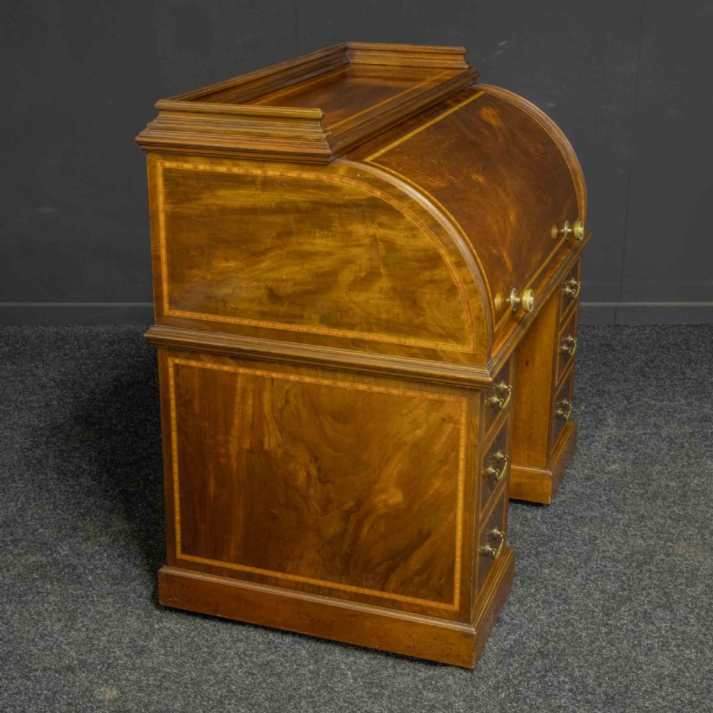 A Sheraton Revival mahogany cylinder desk featuring satinwood crossbanding, twin drawer pedestals, and an extended writing surface fitted with blue leather. View XVI