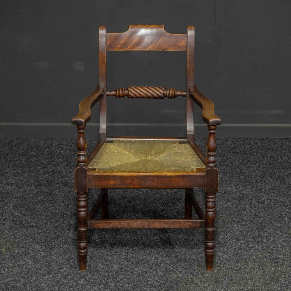 A dark timber provincial Regency armchair featuring a woven rush seat, turned legs, curved arms, and a rope twist back splat.