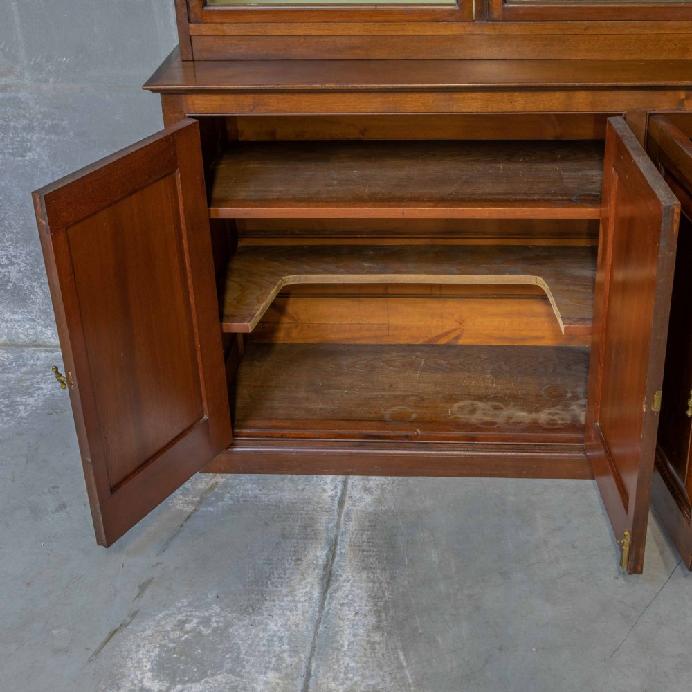 An Edwardian mahogany shop fitting bookcase featuring a three-door glazed upper section with a pale painted interior above a four-door panelled cupboard base. View IV