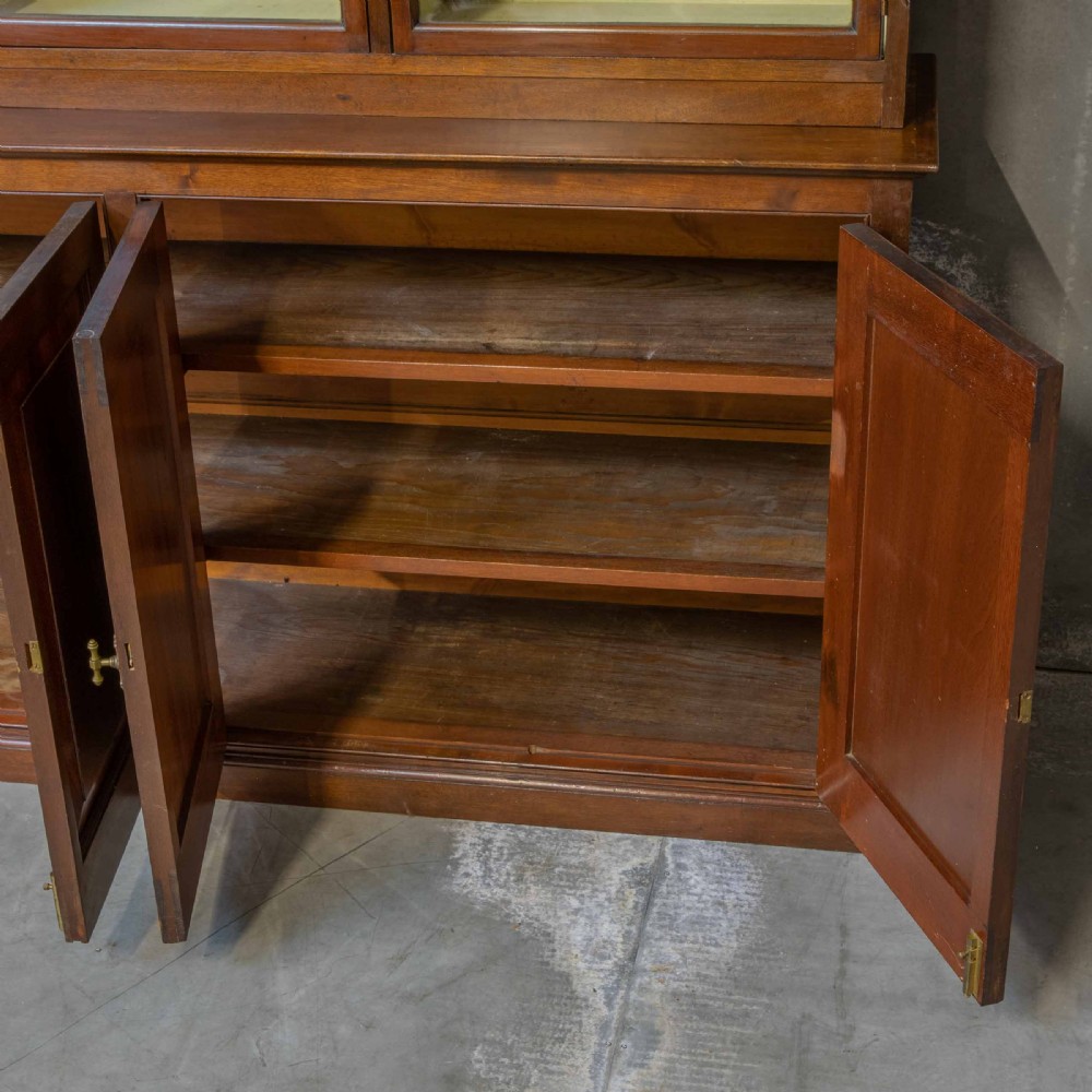 An Edwardian mahogany shop fitting bookcase featuring a three-door glazed upper section with a pale painted interior above a four-door panelled cupboard base. View VI