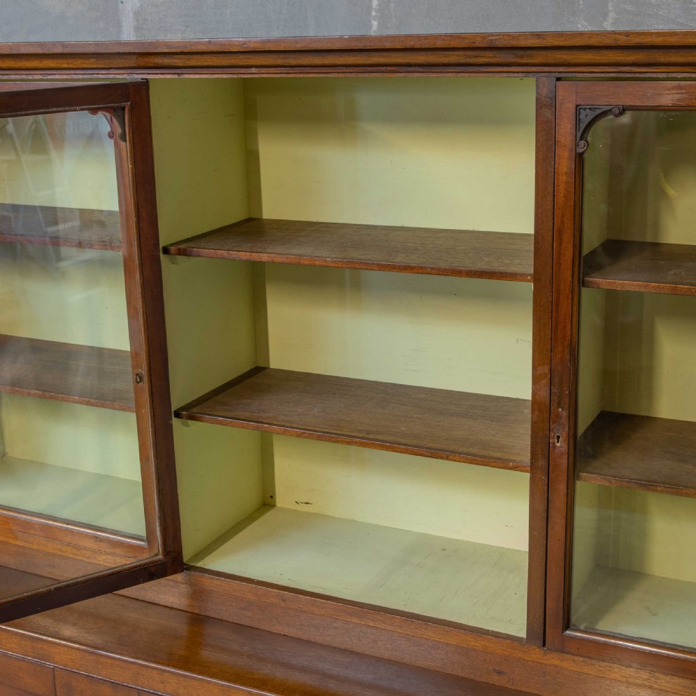 An Edwardian mahogany shop fitting bookcase featuring a three-door glazed upper section with a pale painted interior above a four-door panelled cupboard base. View VII