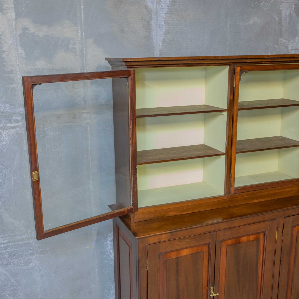 An Edwardian mahogany shop fitting bookcase featuring a three-door glazed upper section with a pale painted interior above a four-door panelled cupboard base. View VIII