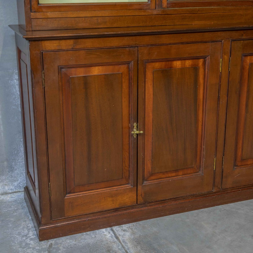 An Edwardian mahogany shop fitting bookcase featuring a three-door glazed upper section with a pale painted interior above a four-door panelled cupboard base. View IX