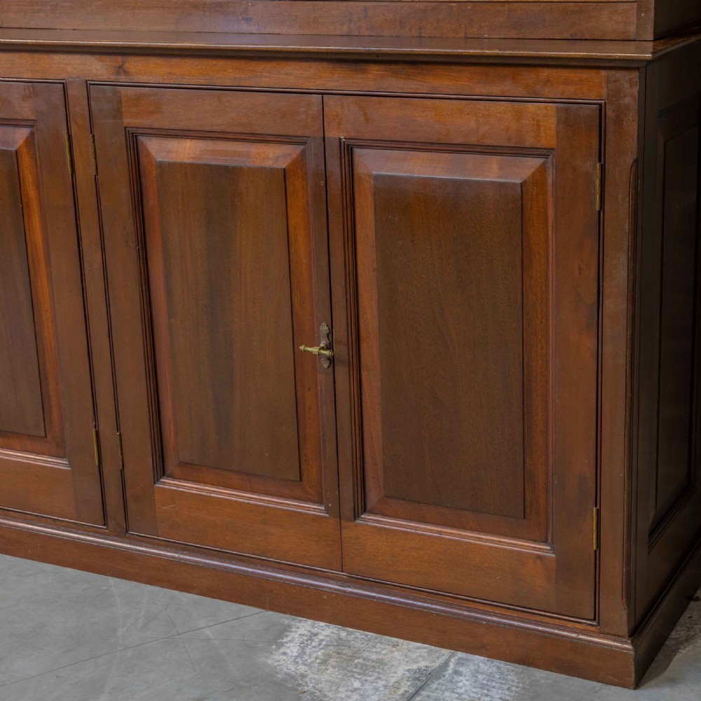 An Edwardian mahogany shop fitting bookcase featuring a three-door glazed upper section with a pale painted interior above a four-door panelled cupboard base. View X
