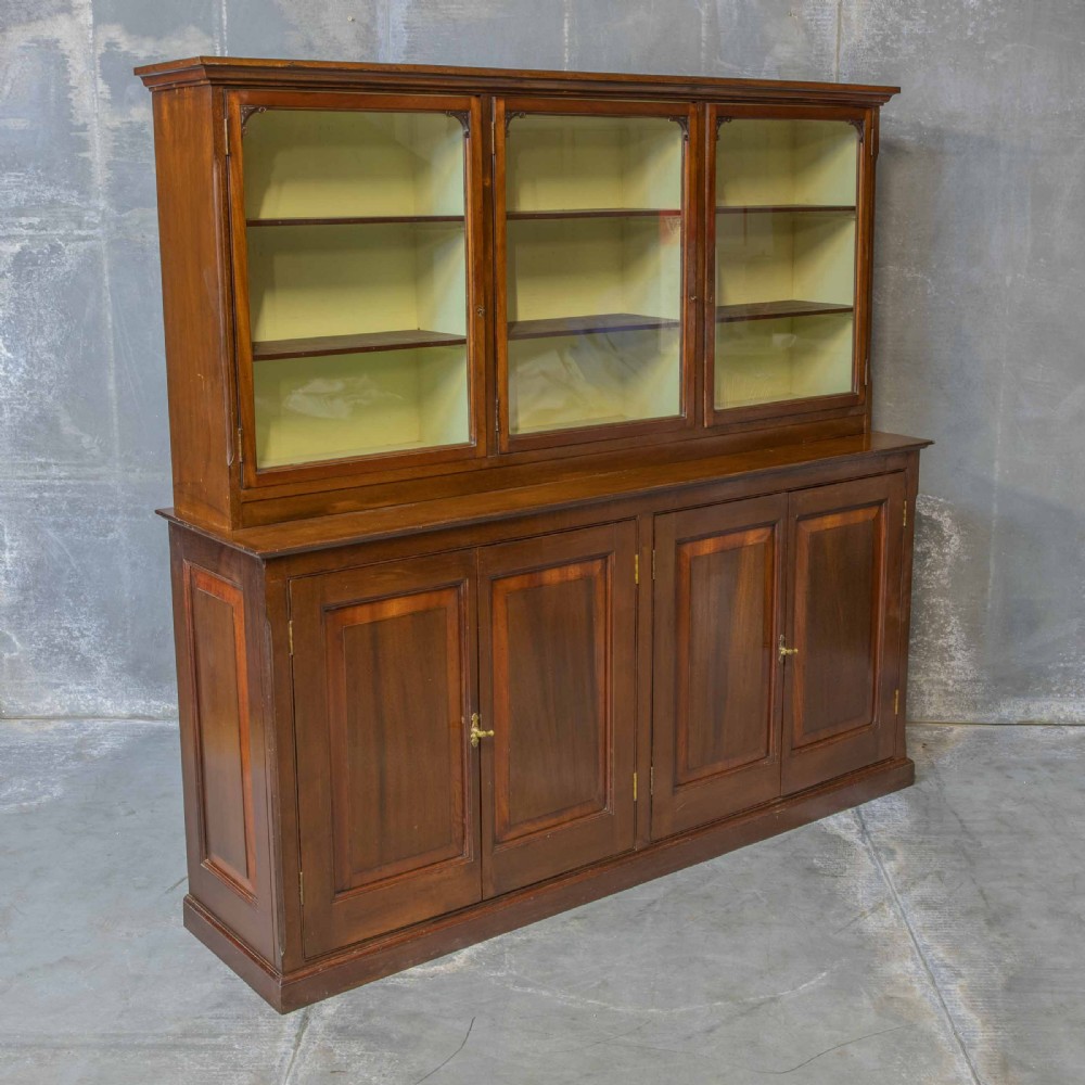 An Edwardian mahogany shop fitting bookcase featuring a three-door glazed upper section with a pale painted interior above a four-door panelled cupboard base. View XV