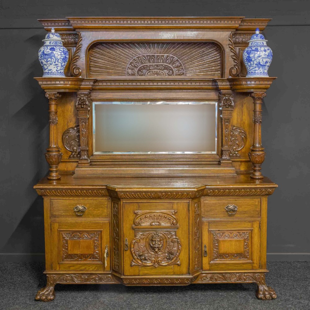 A late Victorian carved oak sideboard with a mirrored backboard superstructure, detailed relief carvings, turned pillars, and claw feet.
