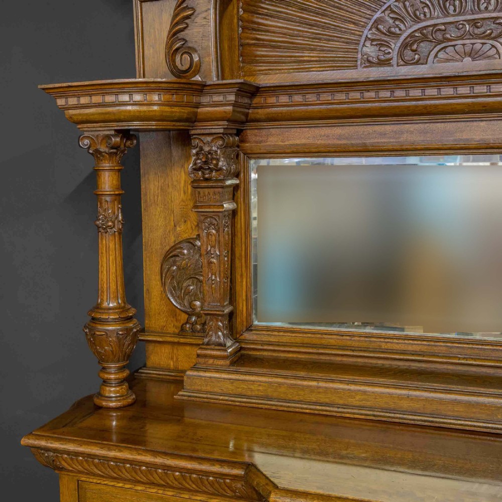 A late Victorian carved oak sideboard with a mirrored backboard superstructure, detailed relief carvings, turned pillars, and claw feet. View IV