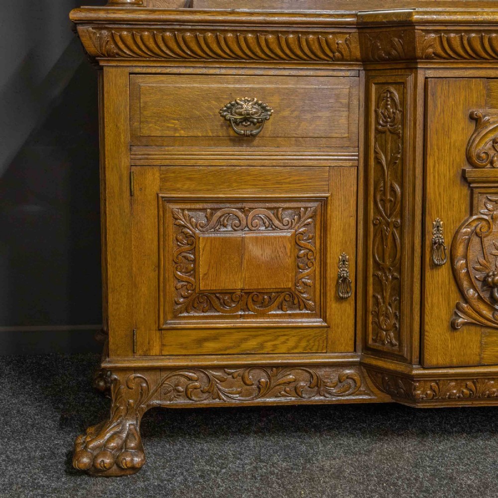 A late Victorian carved oak sideboard with a mirrored backboard superstructure, detailed relief carvings, turned pillars, and claw feet. View VI