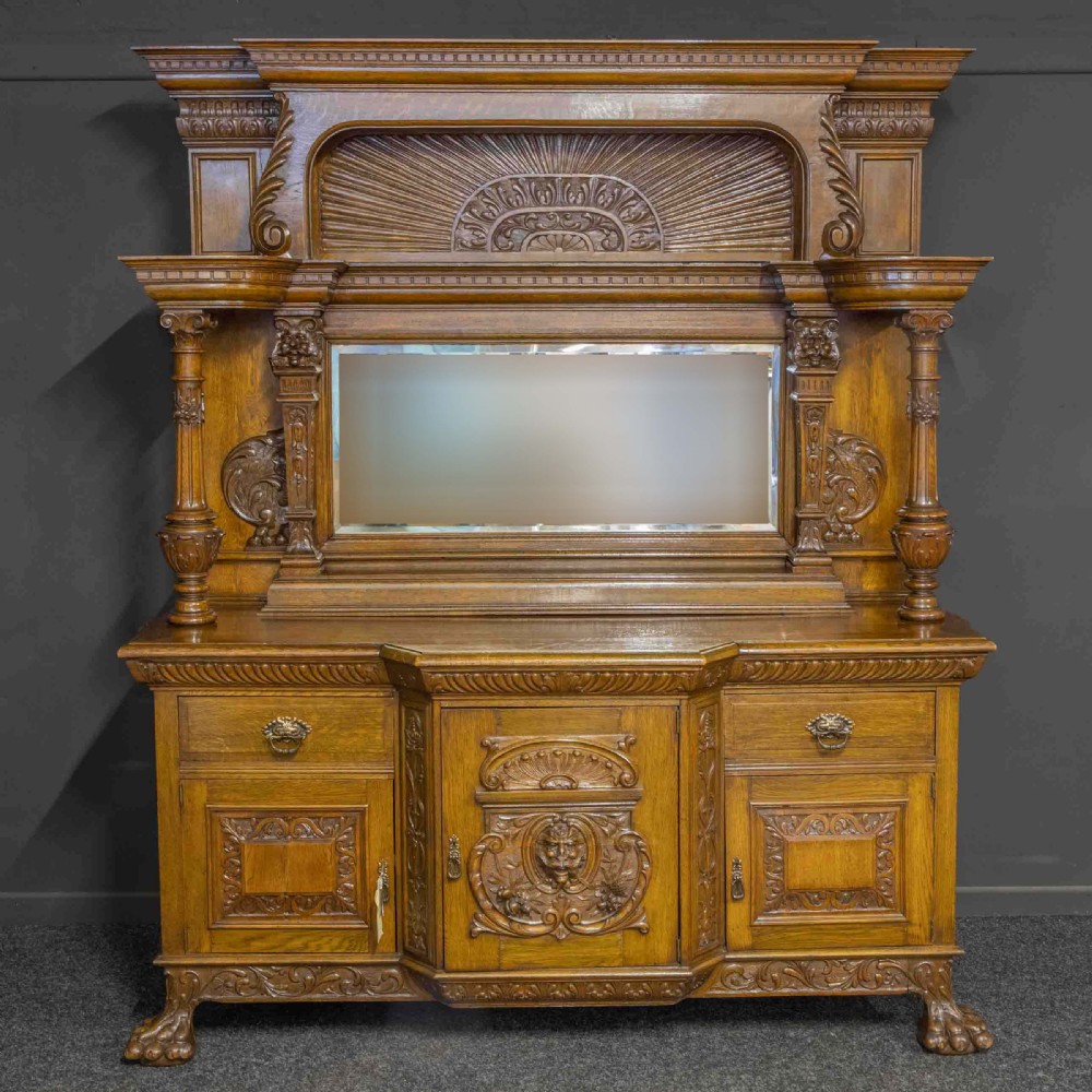 A late Victorian carved oak sideboard with a mirrored backboard superstructure, detailed relief carvings, turned pillars, and claw feet. View VII