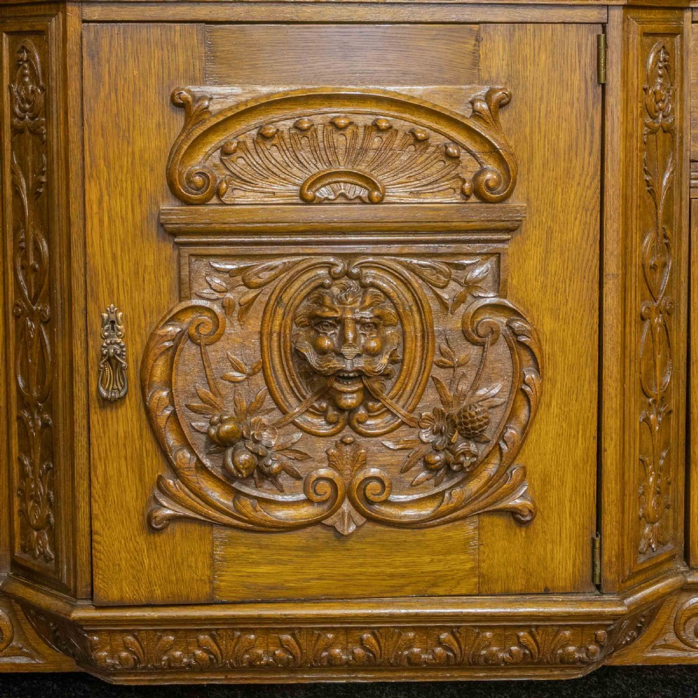 A late Victorian carved oak sideboard with a mirrored backboard superstructure, detailed relief carvings, turned pillars, and claw feet. View VIII