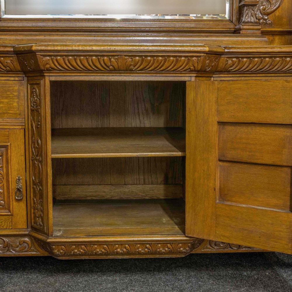 A late Victorian carved oak sideboard with a mirrored backboard superstructure, detailed relief carvings, turned pillars, and claw feet. View IX