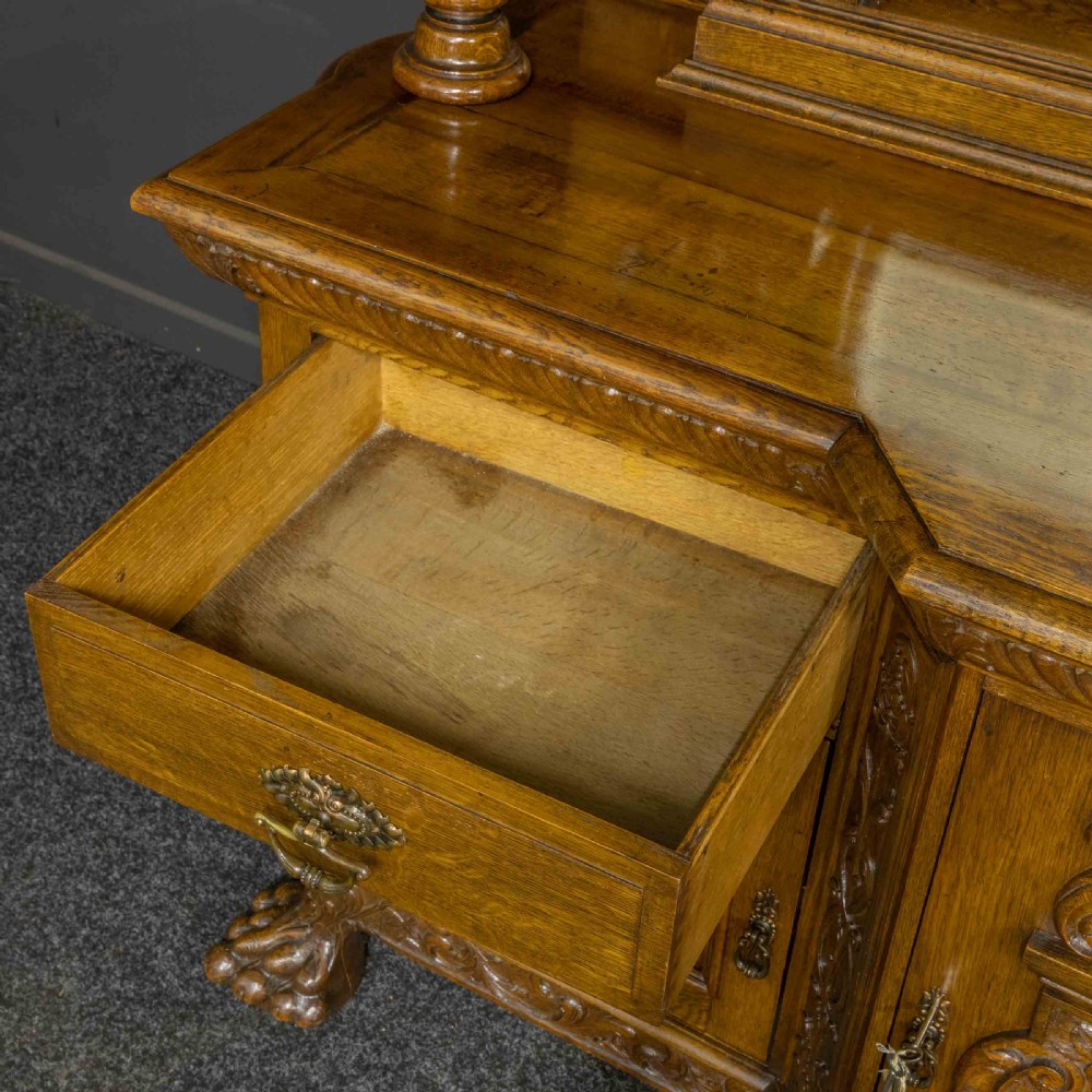 A late Victorian carved oak sideboard with a mirrored backboard superstructure, detailed relief carvings, turned pillars, and claw feet. View XI