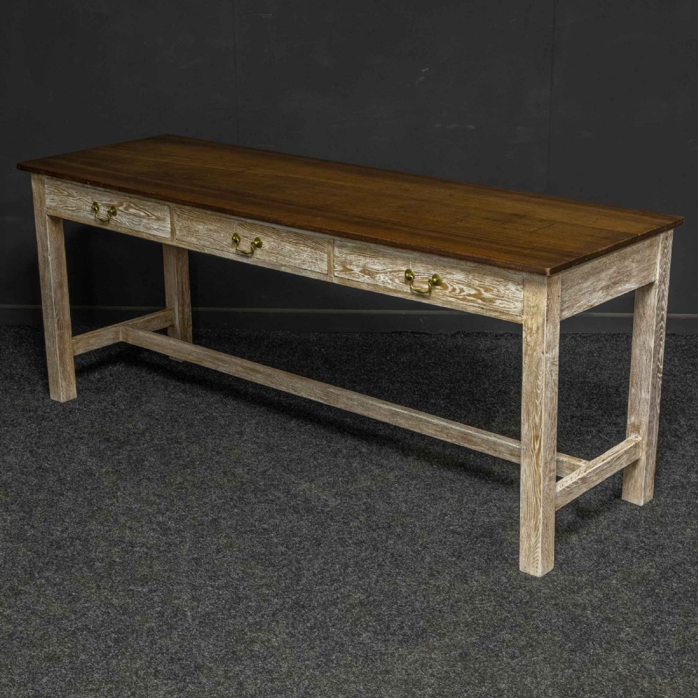 A long early 20th-century wooden console table featuring a polished brown top, whitewashed three-drawer apron, brass drop handles, and straight legs with an H-stretcher. View V