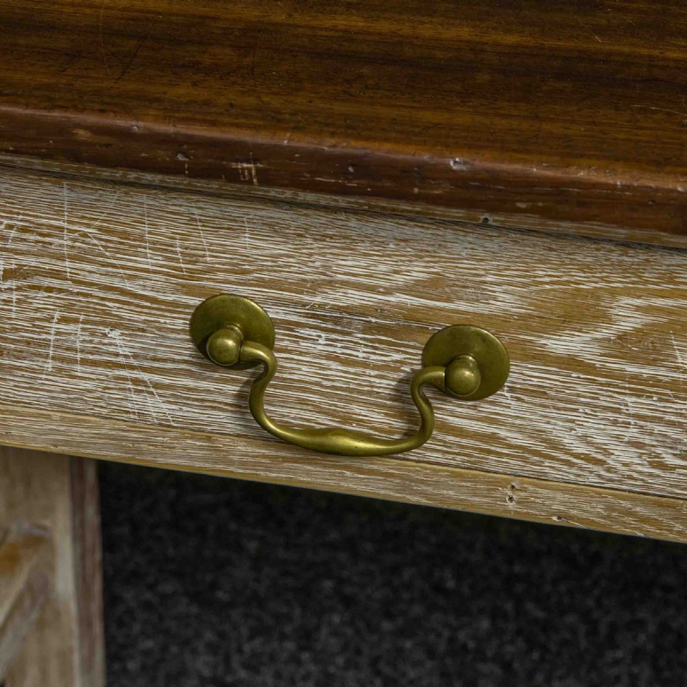 A long early 20th-century wooden console table featuring a polished brown top, whitewashed three-drawer apron, brass drop handles, and straight legs with an H-stretcher. View VII