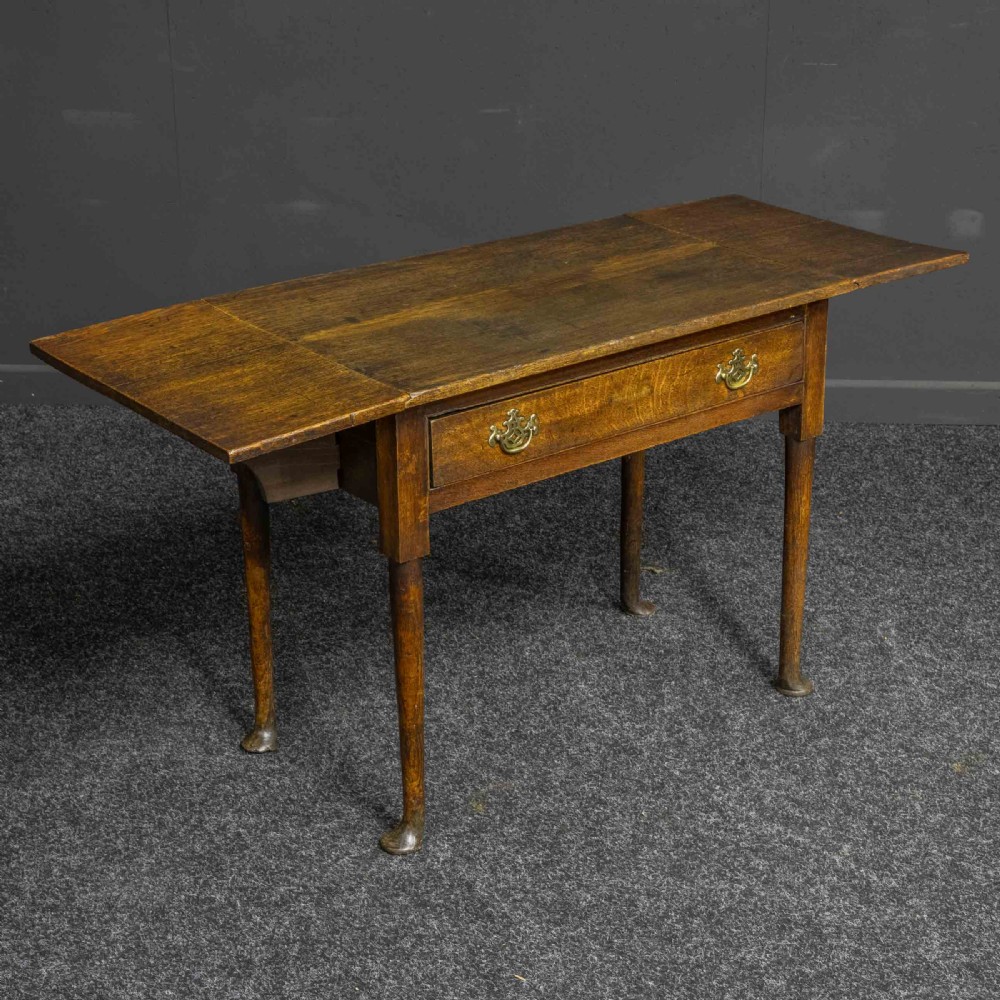A seventeenth-century warm brown oak sofa table featuring side drop-leaf extensions, a single drawer with brass handles, and tapered legs ending in pad feet.