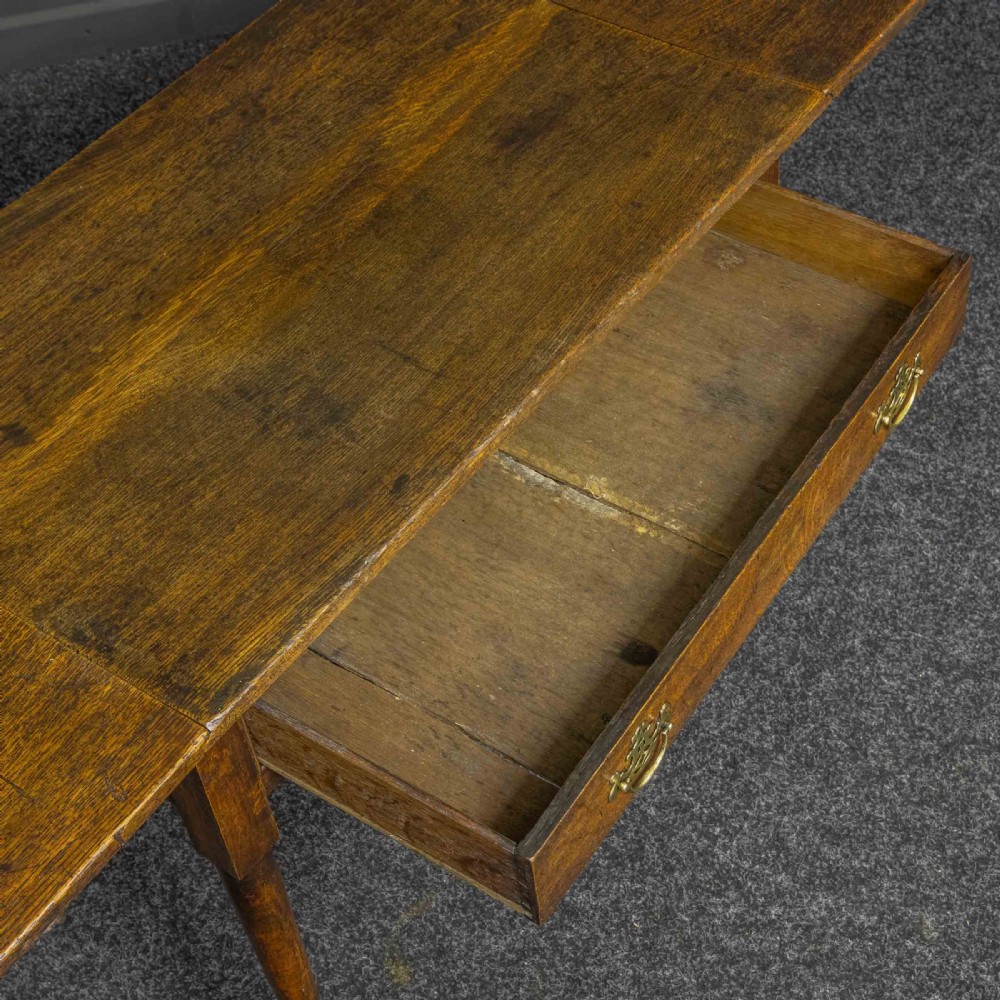 A seventeenth-century warm brown oak sofa table featuring side drop-leaf extensions, a single drawer with brass handles, and tapered legs ending in pad feet. View V