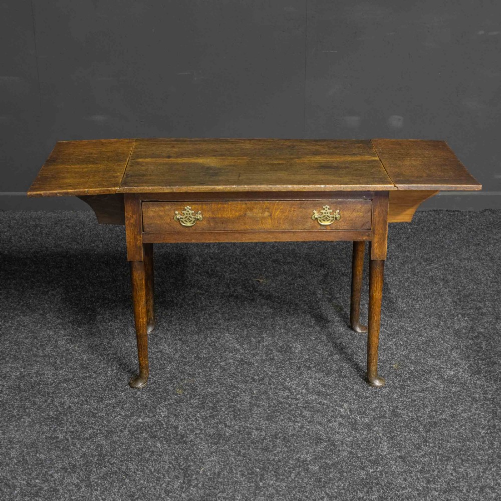 A seventeenth-century warm brown oak sofa table featuring side drop-leaf extensions, a single drawer with brass handles, and tapered legs ending in pad feet. View VI