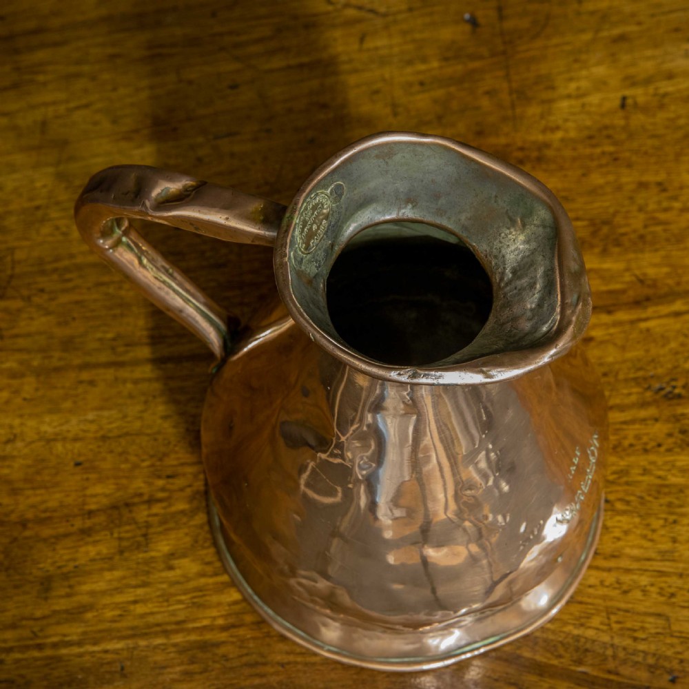 A nineteenth-century copper ale flagon featuring a conical body, a broad curved strap handle, and stamped verification marks inside the lip. View III