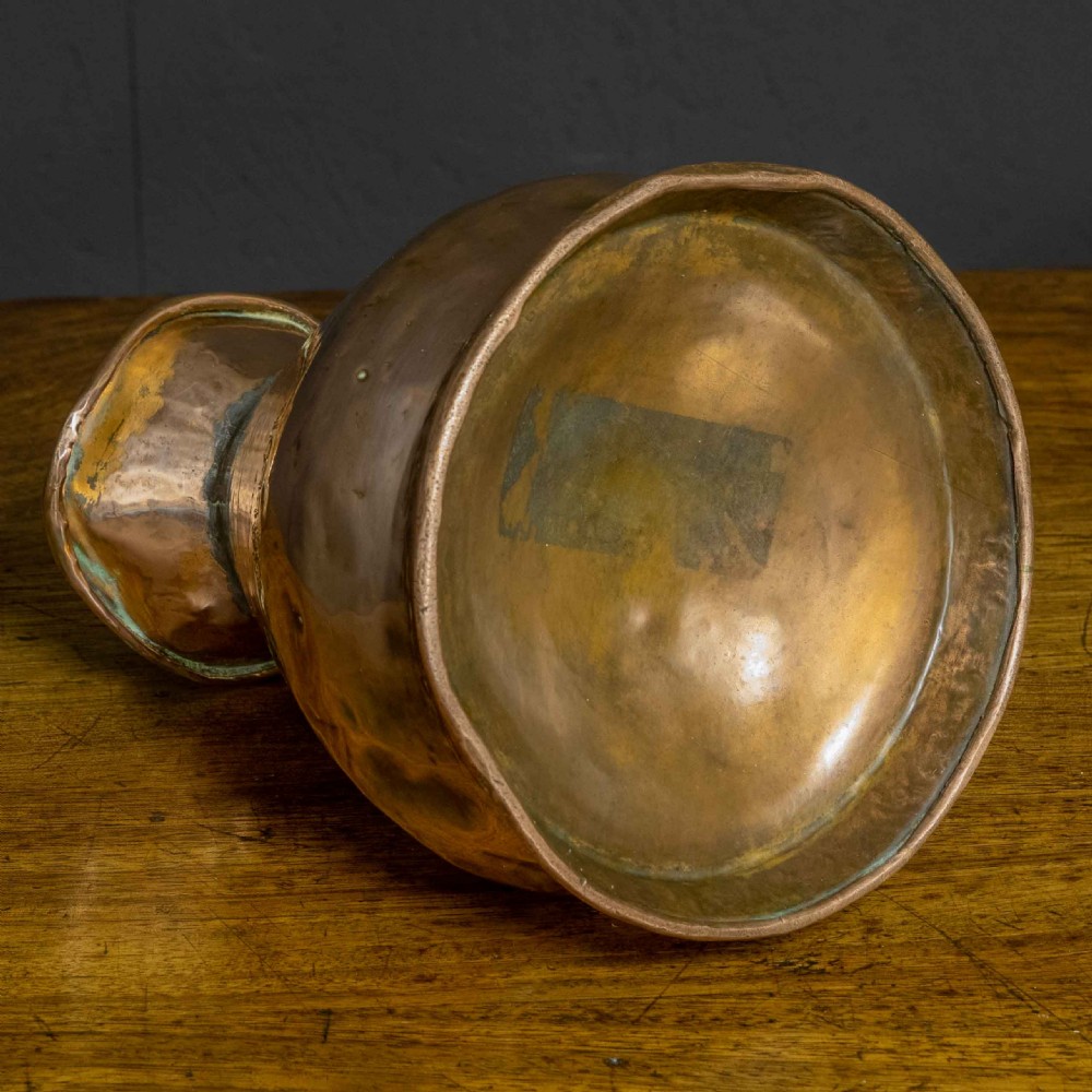 A nineteenth-century copper ale flagon featuring a conical body, a broad curved strap handle, and stamped verification marks inside the lip. View VIII