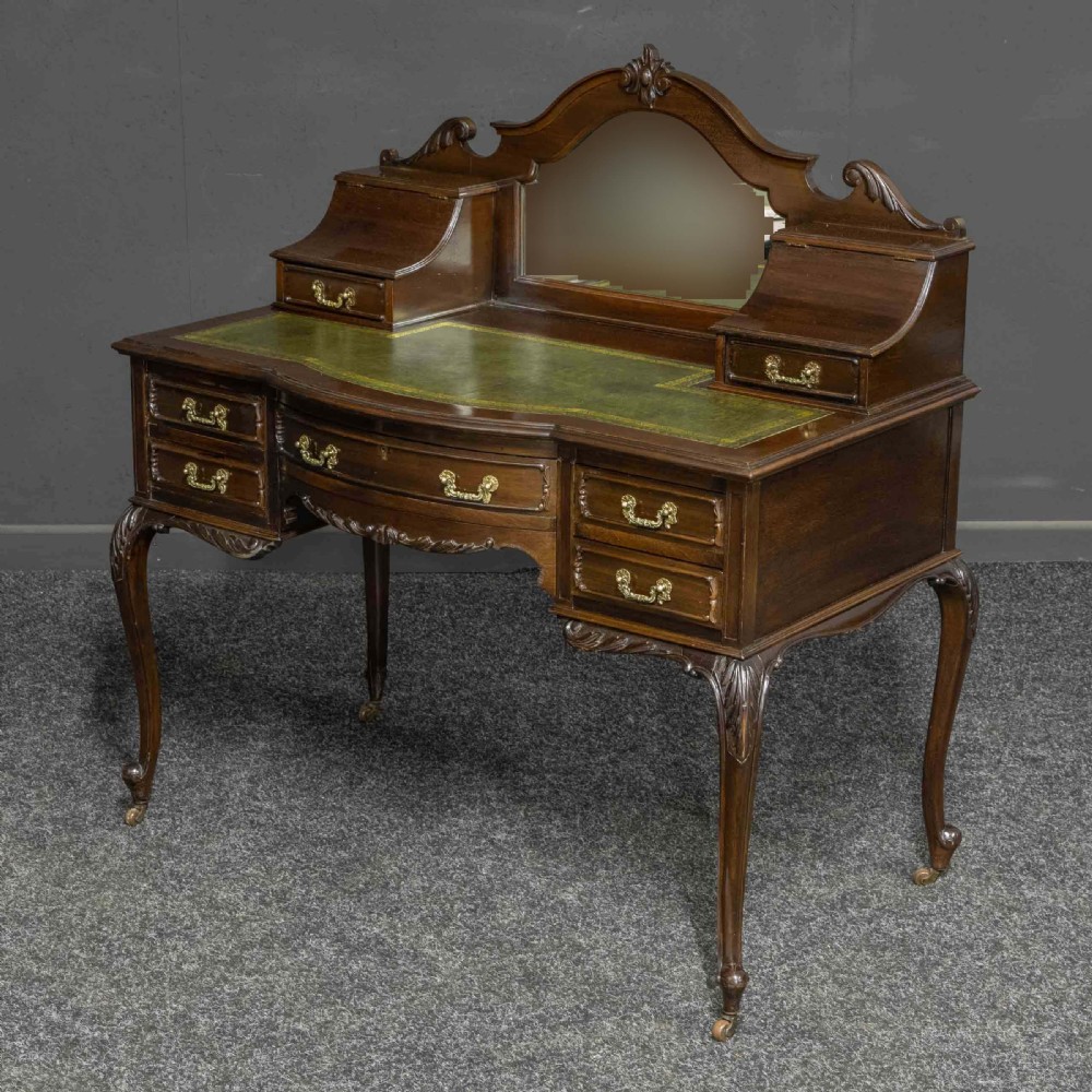 A late Victorian dark mahogany ladies writing desk featuring a green leather inset top, raised mirror superstructure, small side drawers, carved cabriole legs, and brass handles.