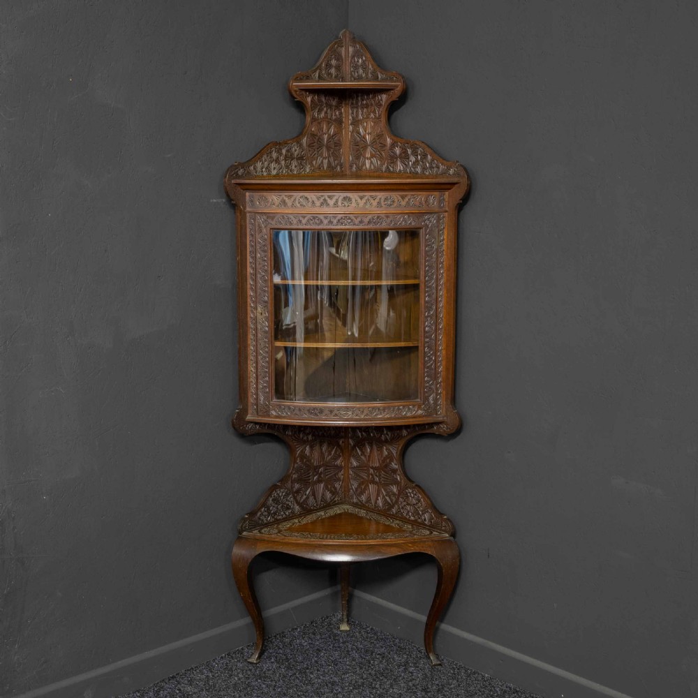 Carved dark walnut corner display cabinet featuring a single glazed door, decorative carved panels, upper and lower shelves, and cabriole legs.