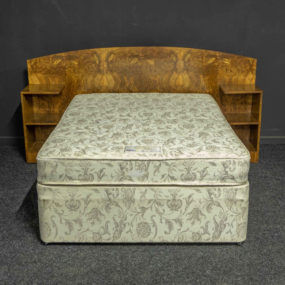 An Art Deco burr walnut headboard featuring a gently arched crest and integrated open bedside shelves on both sides.