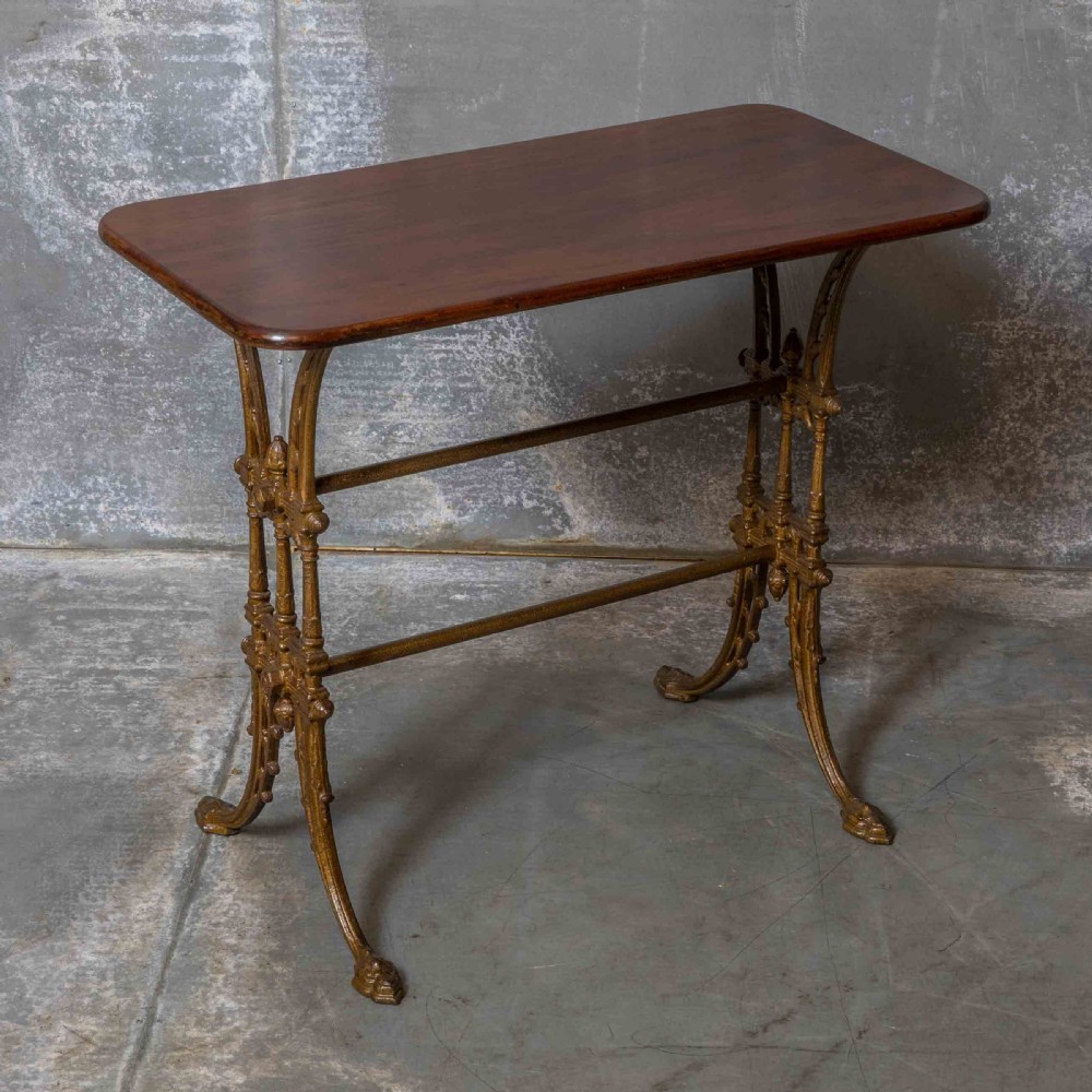 A rectangular dark wood tabletop mounted on a gold-painted cast iron base with stretchers and ornamental feet.
