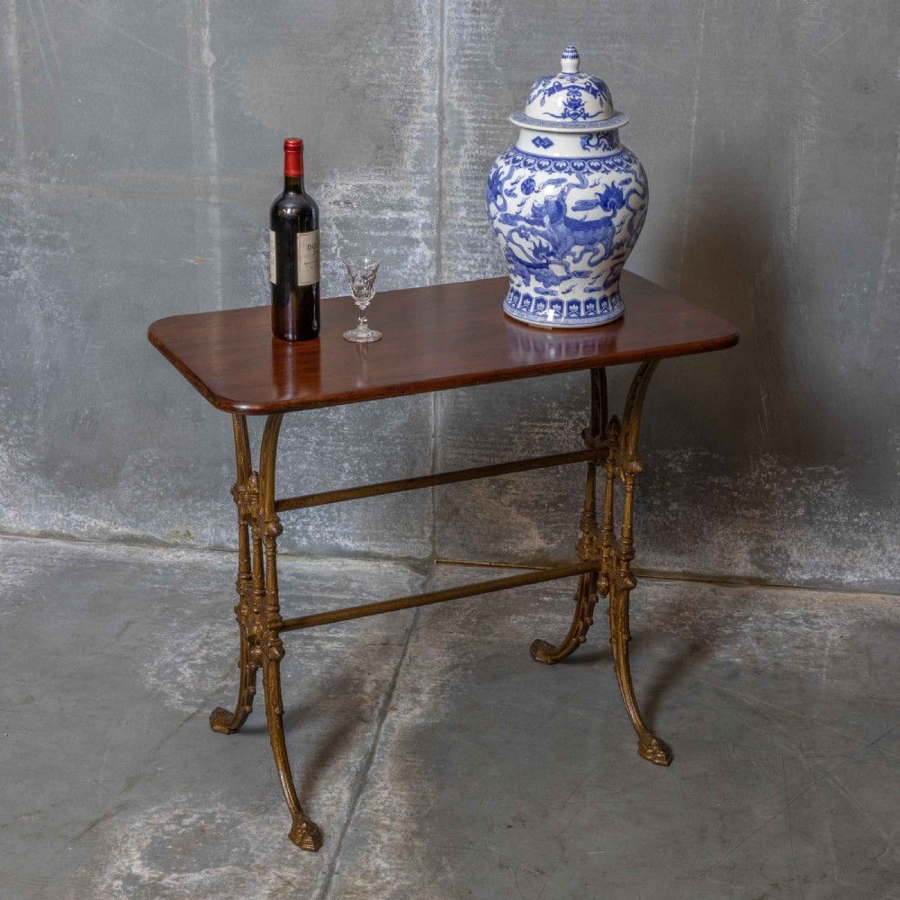 A rectangular dark wood tabletop mounted on a gold-painted cast iron base with stretchers and ornamental feet. View II