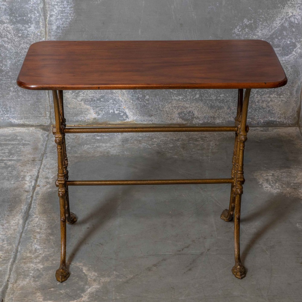 A rectangular dark wood tabletop mounted on a gold-painted cast iron base with stretchers and ornamental feet. View III