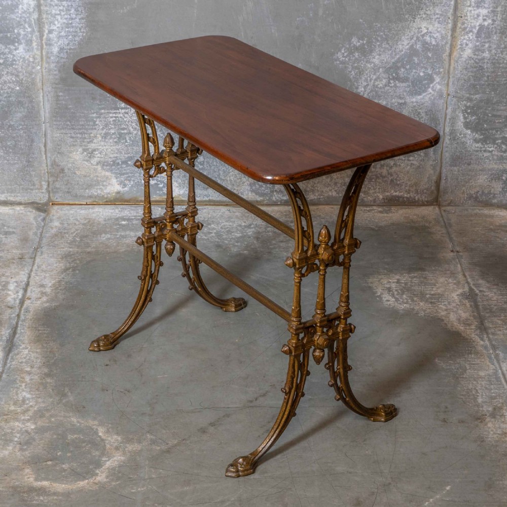 A rectangular dark wood tabletop mounted on a gold-painted cast iron base with stretchers and ornamental feet. View IV
