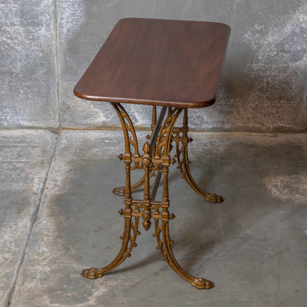 A rectangular dark wood tabletop mounted on a gold-painted cast iron base with stretchers and ornamental feet. View V