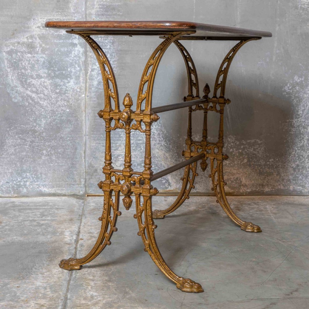 A rectangular dark wood tabletop mounted on a gold-painted cast iron base with stretchers and ornamental feet. View VII