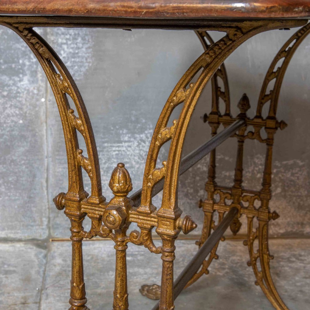 A rectangular dark wood tabletop mounted on a gold-painted cast iron base with stretchers and ornamental feet. View IX