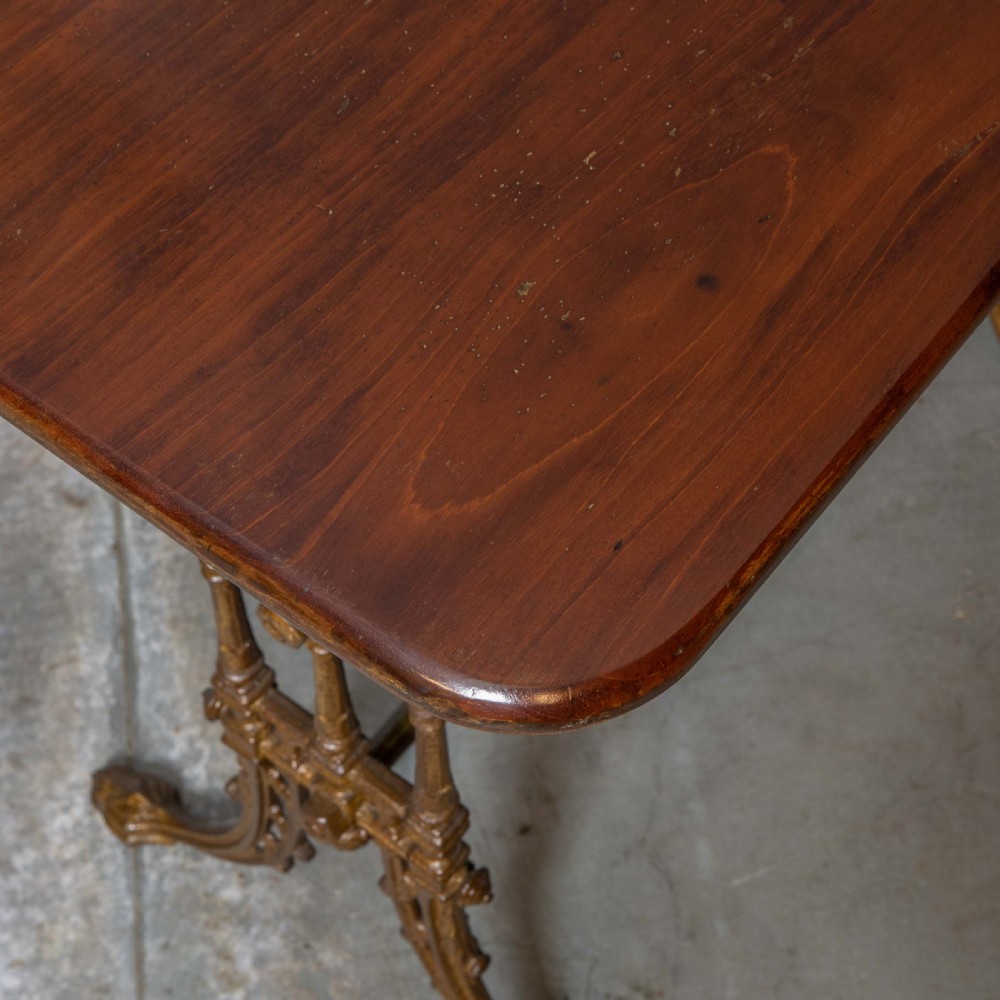 A rectangular dark wood tabletop mounted on a gold-painted cast iron base with stretchers and ornamental feet. View X