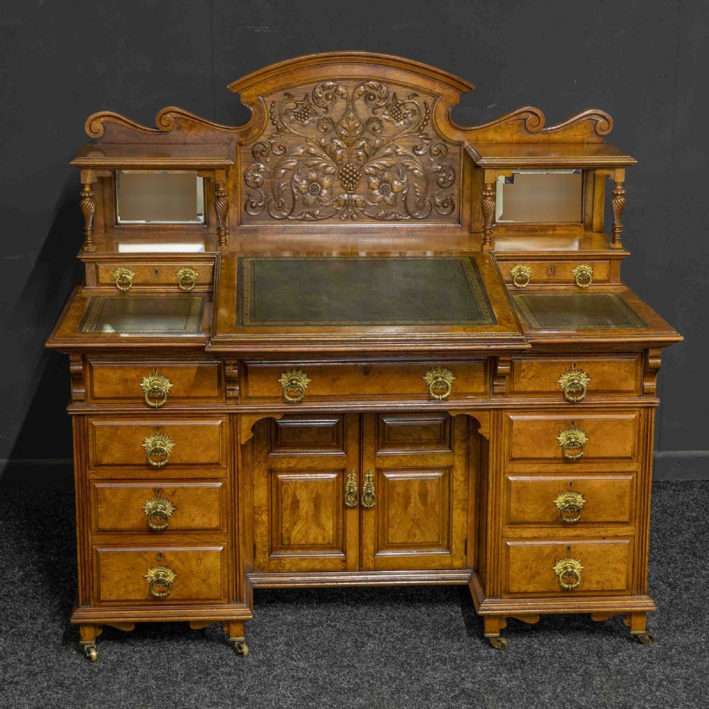 A late Victorian pollard oak desk featuring a central sloped green leather writing surface, carved backboard cresting, tiered shelves with mirrors, and brass-handled drawers. View II