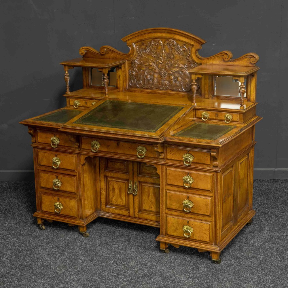 A late Victorian pollard oak desk featuring a central sloped green leather writing surface, carved backboard cresting, tiered shelves with mirrors, and brass-handled drawers. View III