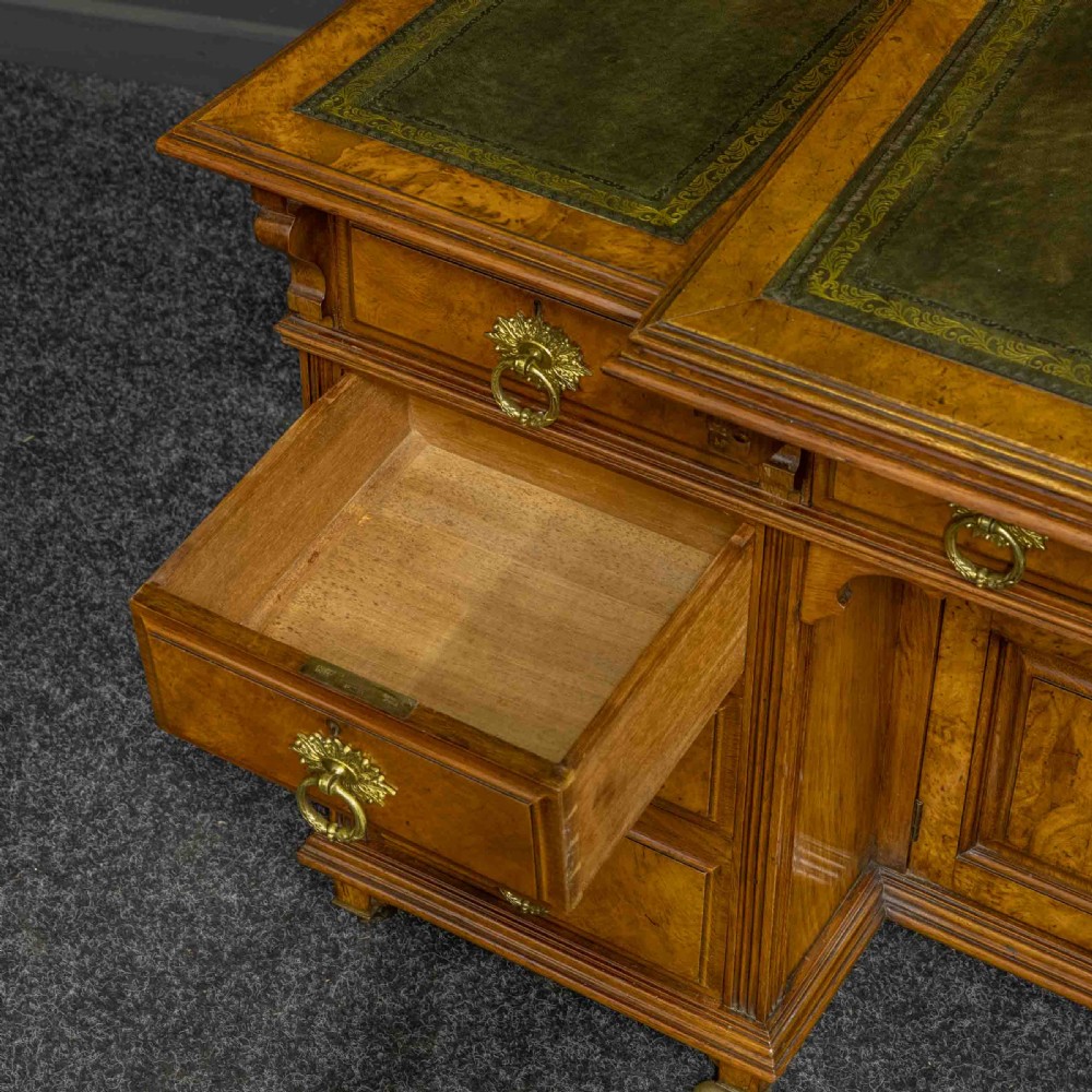 A late Victorian pollard oak desk featuring a central sloped green leather writing surface, carved backboard cresting, tiered shelves with mirrors, and brass-handled drawers. View X