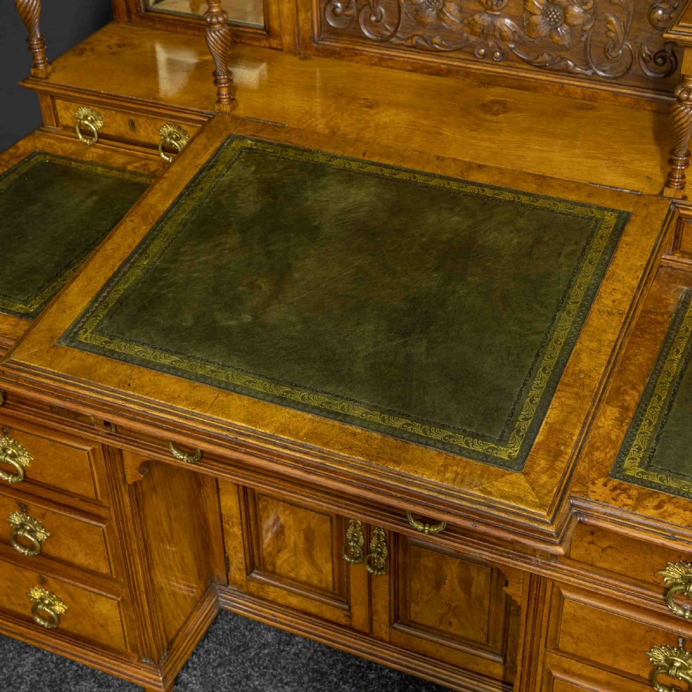 A late Victorian pollard oak desk featuring a central sloped green leather writing surface, carved backboard cresting, tiered shelves with mirrors, and brass-handled drawers. View XIV