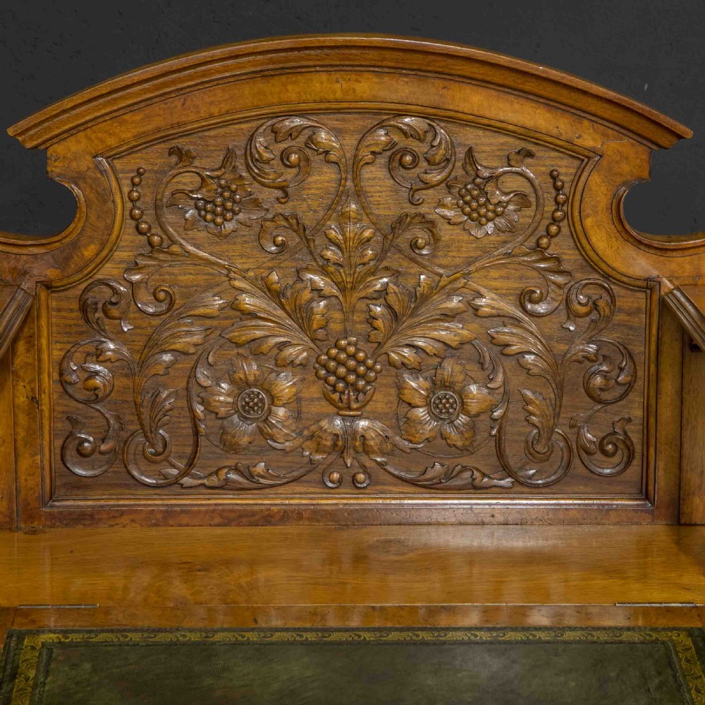 A late Victorian pollard oak desk featuring a central sloped green leather writing surface, carved backboard cresting, tiered shelves with mirrors, and brass-handled drawers. View XVI
