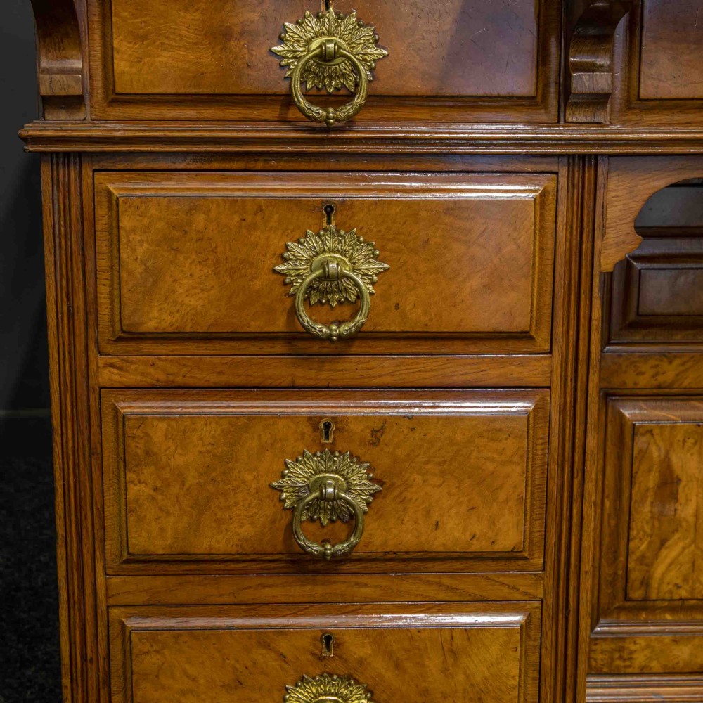 A late Victorian pollard oak desk featuring a central sloped green leather writing surface, carved backboard cresting, tiered shelves with mirrors, and brass-handled drawers. View XVII