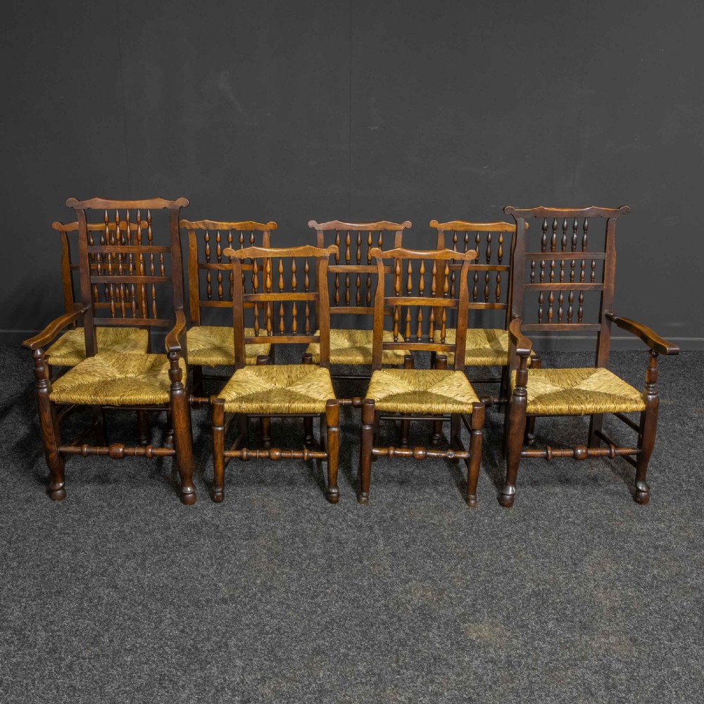 A set of eight Georgian dark oak spindleback dining chairs featuring two carver armchairs and six single side chairs with woven rush seats.